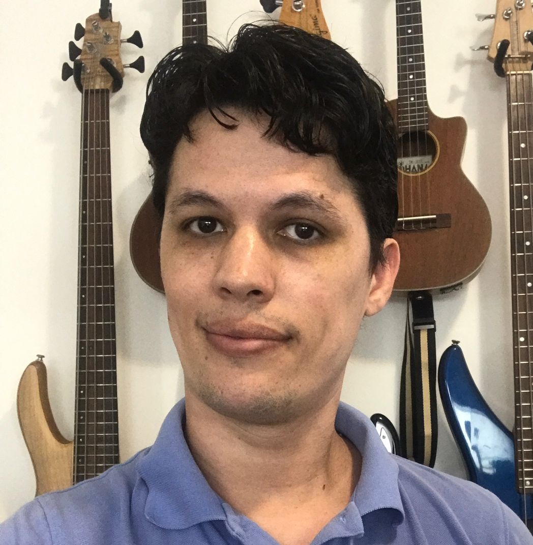 Ale Hilário, professor de música, ao fundo instrumentos pendurados na parede